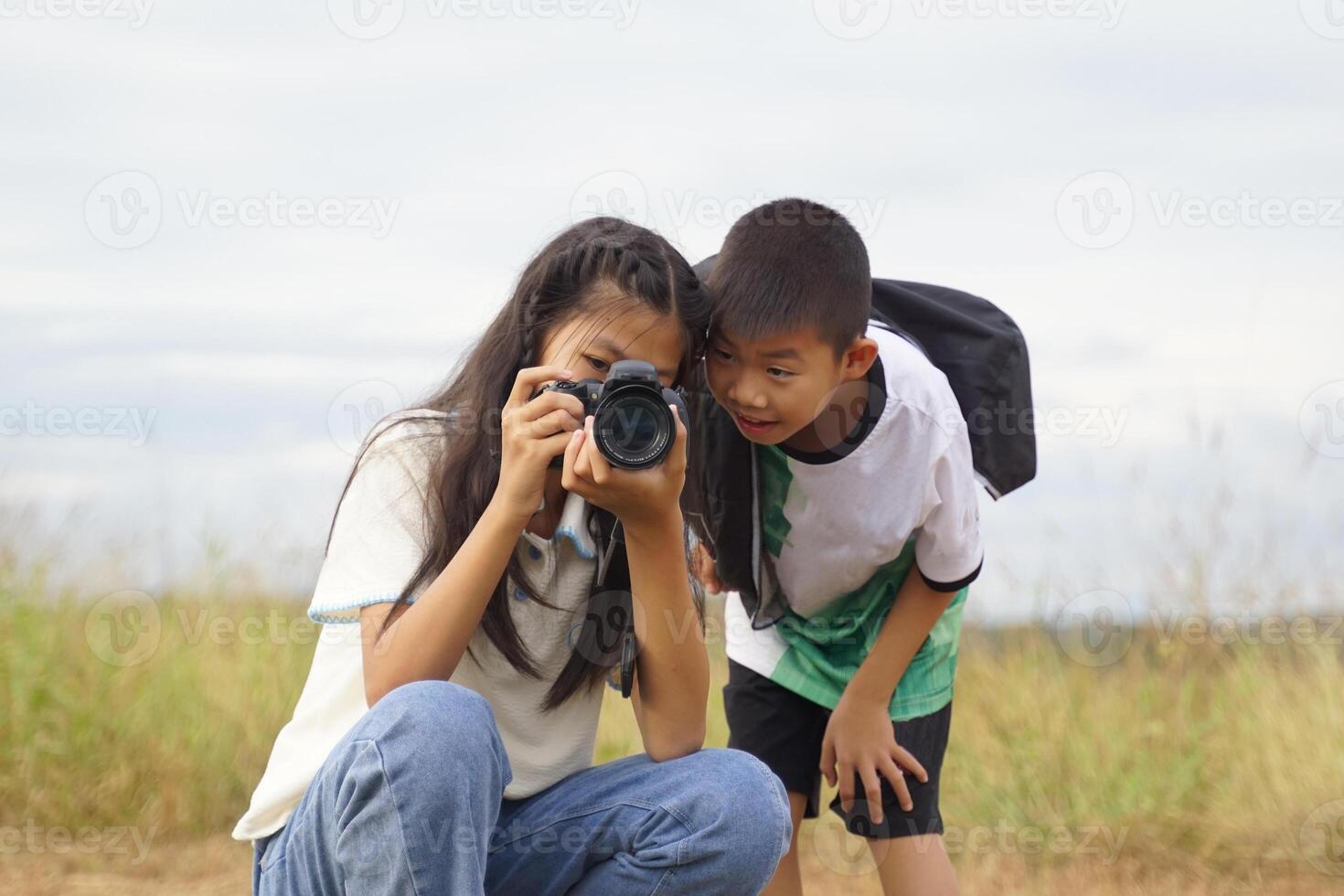 Asian boy and girl use digital camera to take nature photos in the field in their free time. Concept of exploration, outside the classroom, outdoors, ecology, nature, learning, travel.