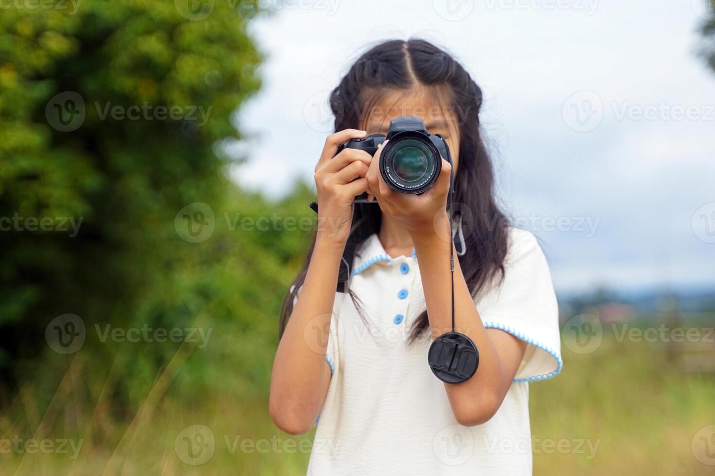 Asian girl uses digital camera to take photos of nature in a field. Concept of exploration, outside the classroom, outdoors, ecology, nature, learning, travel.