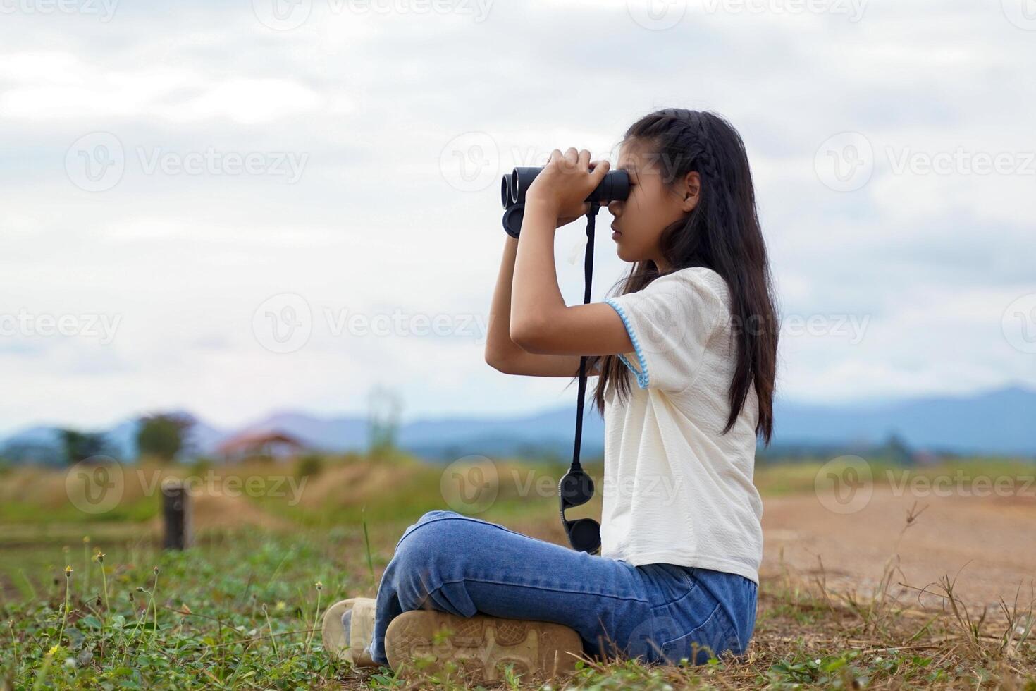 Asian girl uses binoculars to explore nature in the field. the concept of learning outside the classroom nature study, exploration. photo