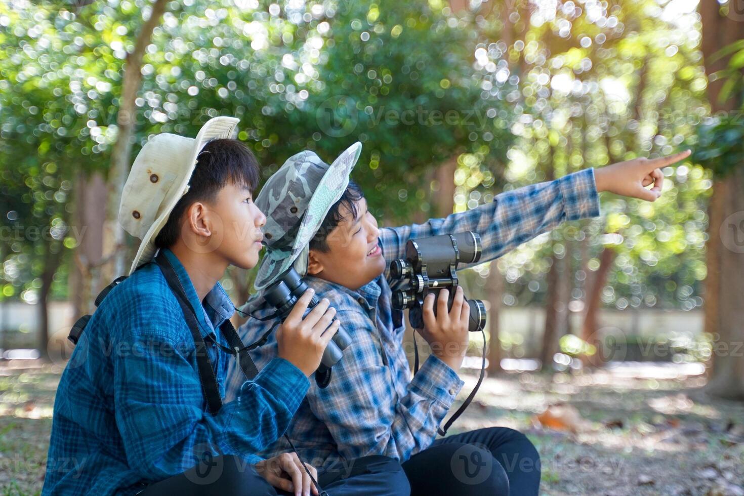 Two Asian boys use binoculars to study the local birds in a community forest. Soft and selective focus. photo