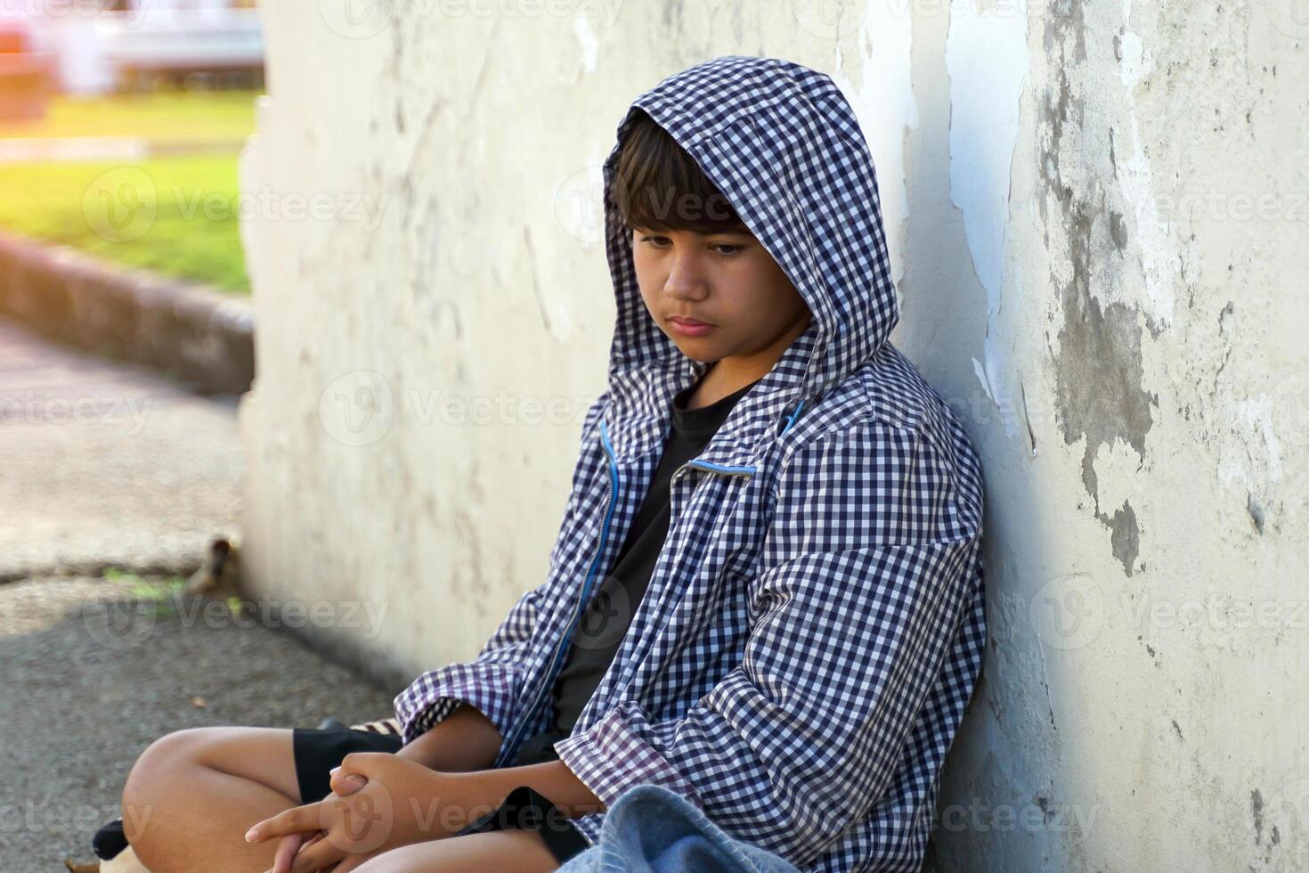 homeless young man with a hood over his head sits leaning against a wall. concept of homelessness, abandonment, sad, lonely, hopeless, depressed. photo