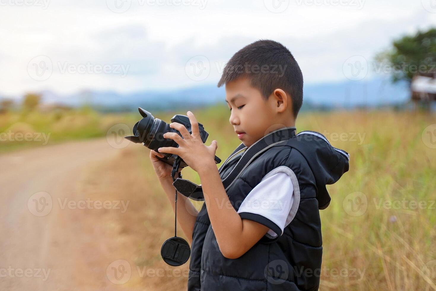 Asian boy uses digital camera to take nature photos in a field. Concept of exploration, outside the classroom, outdoors, ecology, nature, learning, travel.