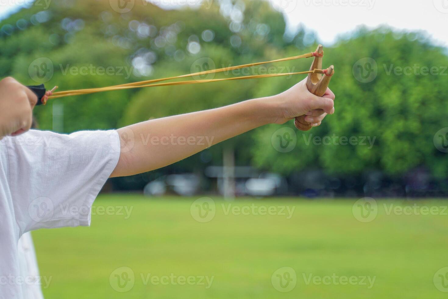 Hand holding Slingshot on green background It is a weapon made from a forked stick with rubber attached to a leather strip that holds bullets to be fired. photo