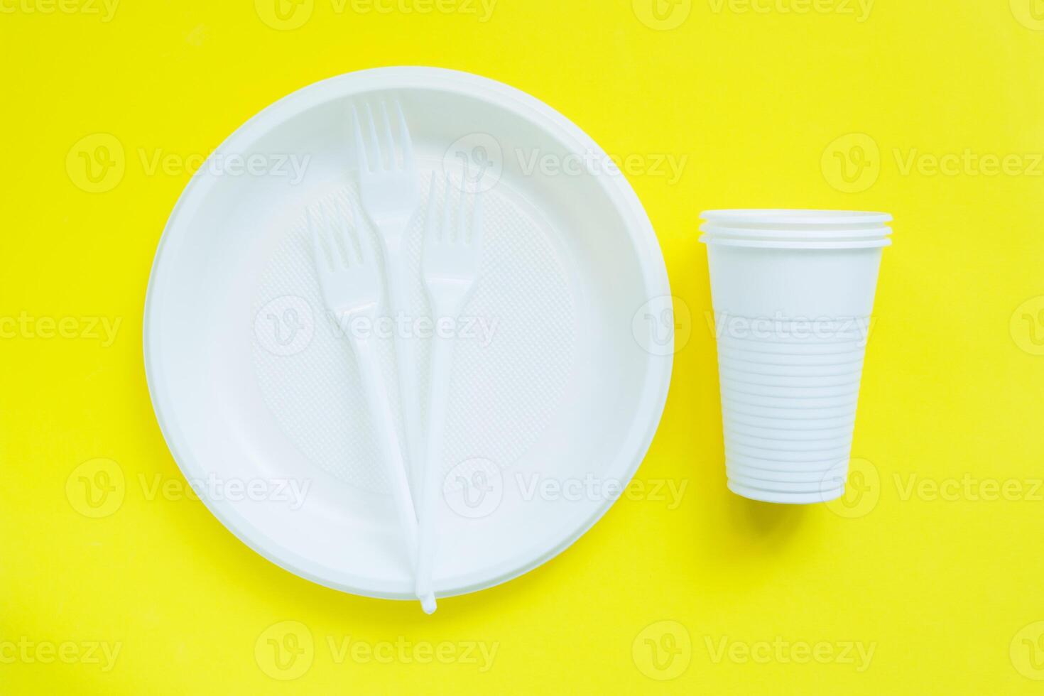 Disposable plastic tableware on bright yellow background. Non-ecological use photo