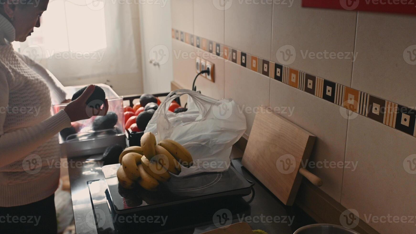Woman Unpacking Fresh Avocados, Bananas, and Tomatoes in a Kitchen photo