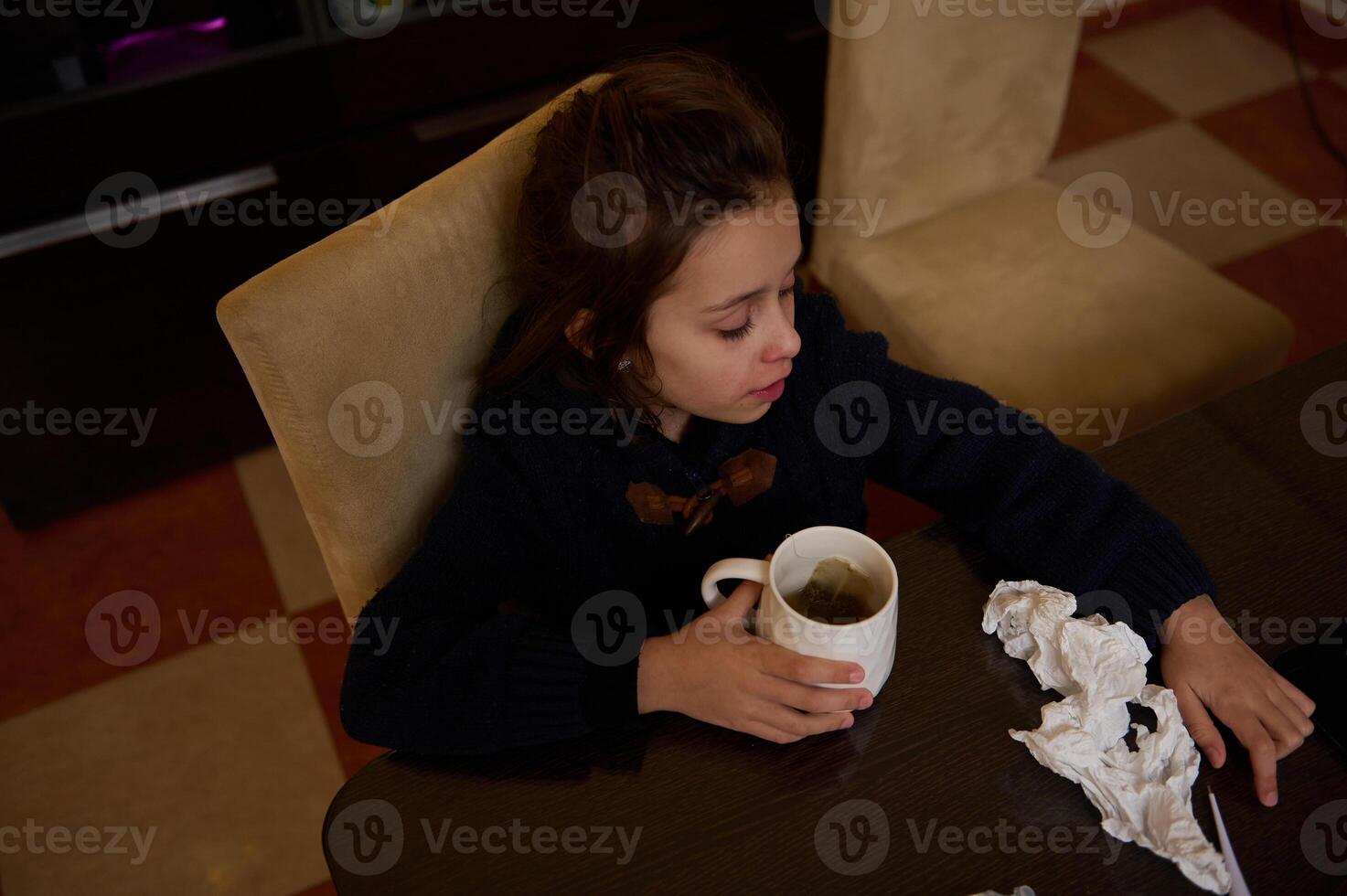 Young girl drinking tea at a table with tissues and a cozy atmosphere photo