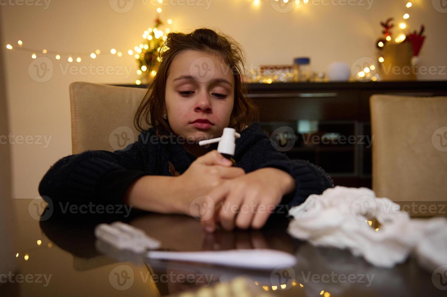 Child holding medical nasal spray with tissue on table photo