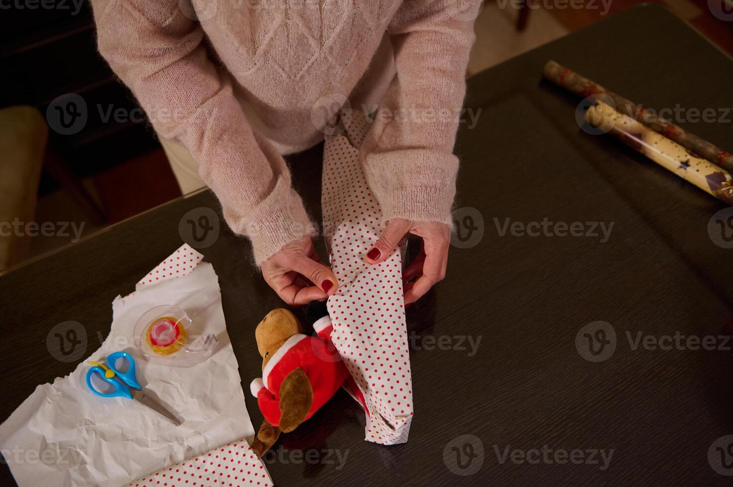 Wrapping a toy teddy in festive paper on a wooden table photo