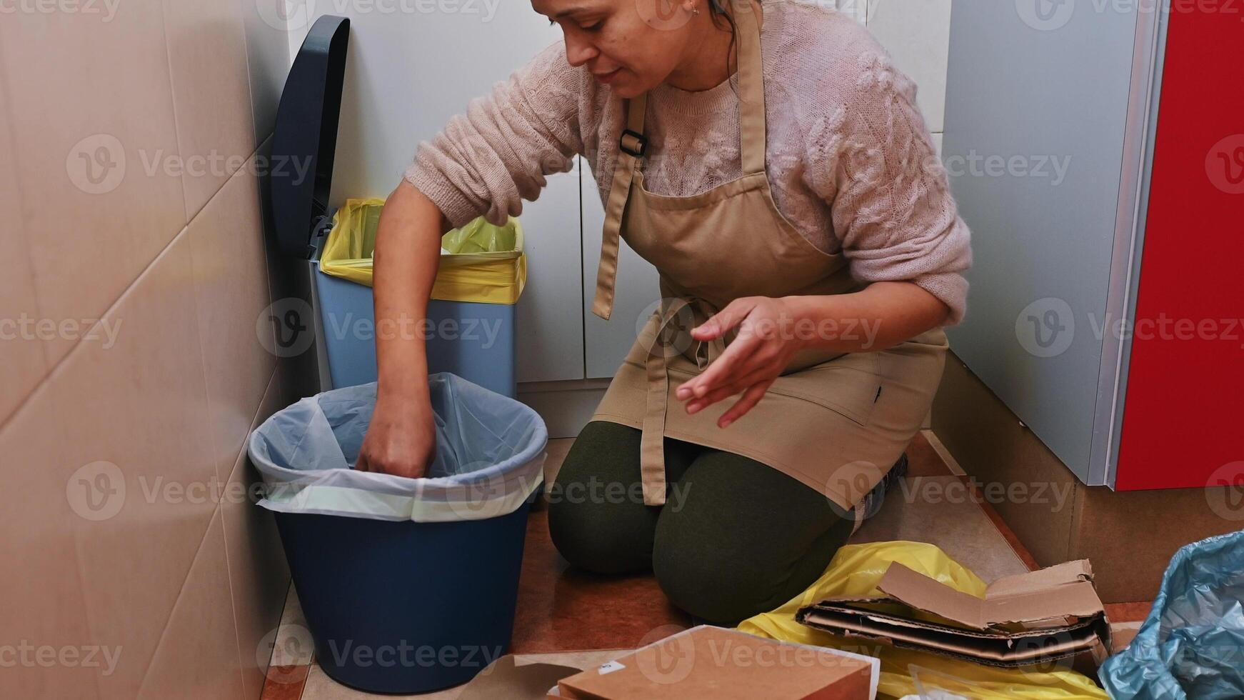 Woman sorting and disposing of waste in a kitchen with recycling bins photo