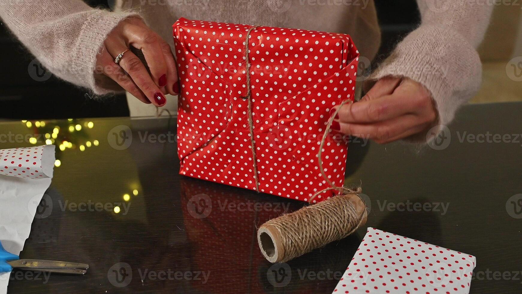 Woman Wrapping Christmas Gifts with Festive Red Polka Dot Paper and String photo