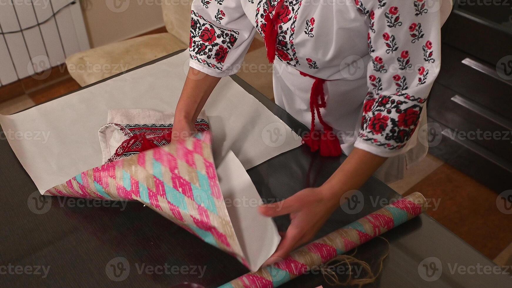 Person wrapping traditional embroidered fabric with decorative paper on a table photo