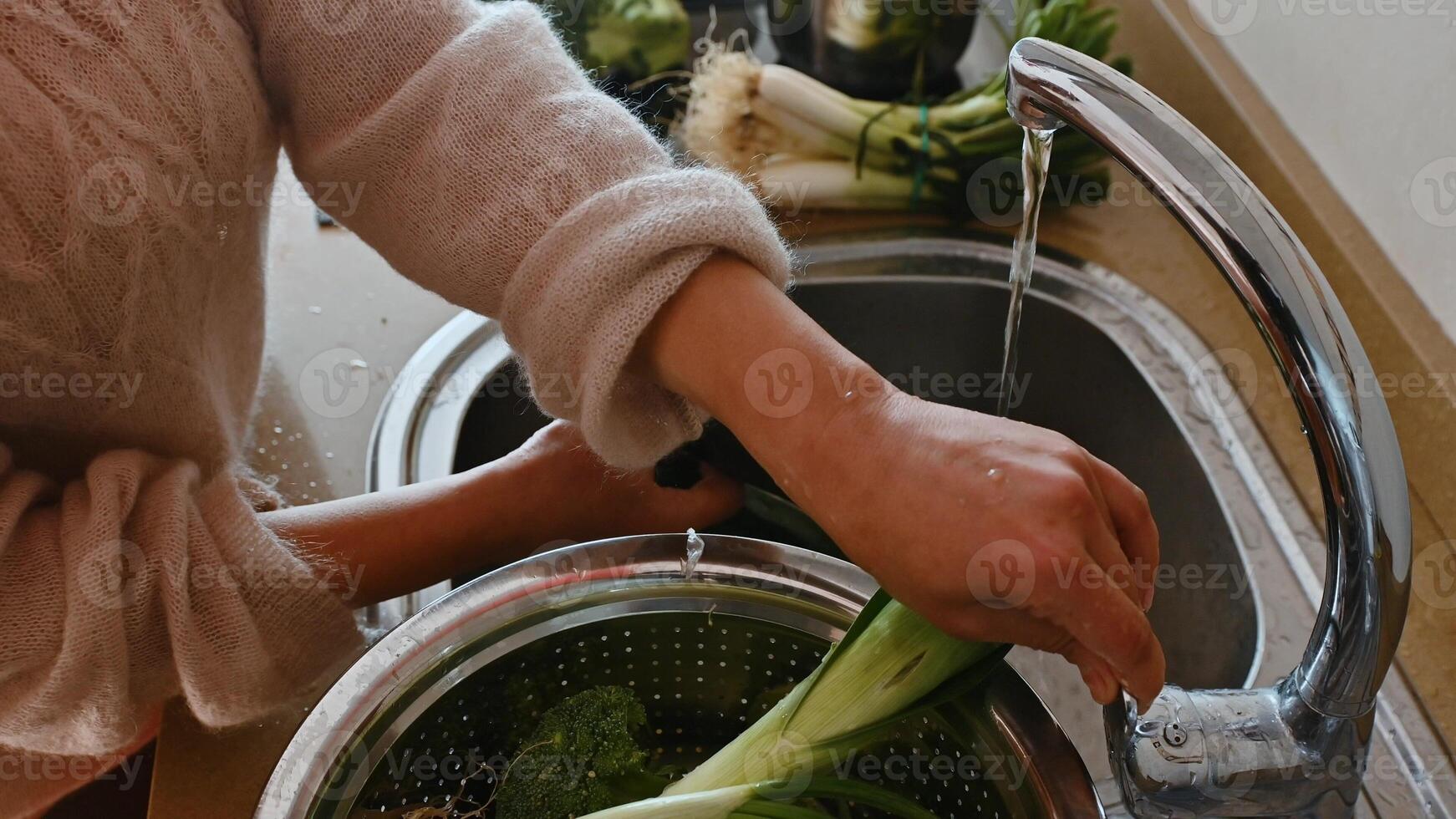 Person washing vegetables under running water in a kitchen sink photo