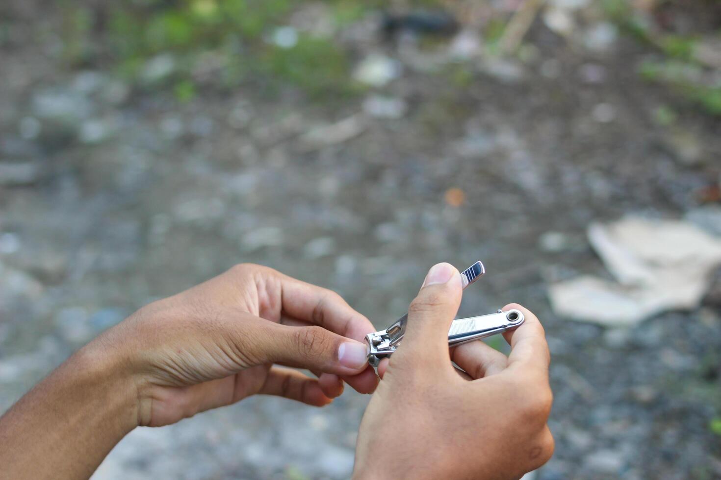 close up of a teenager's hand cutting nails with a nail clipper outdoors photo