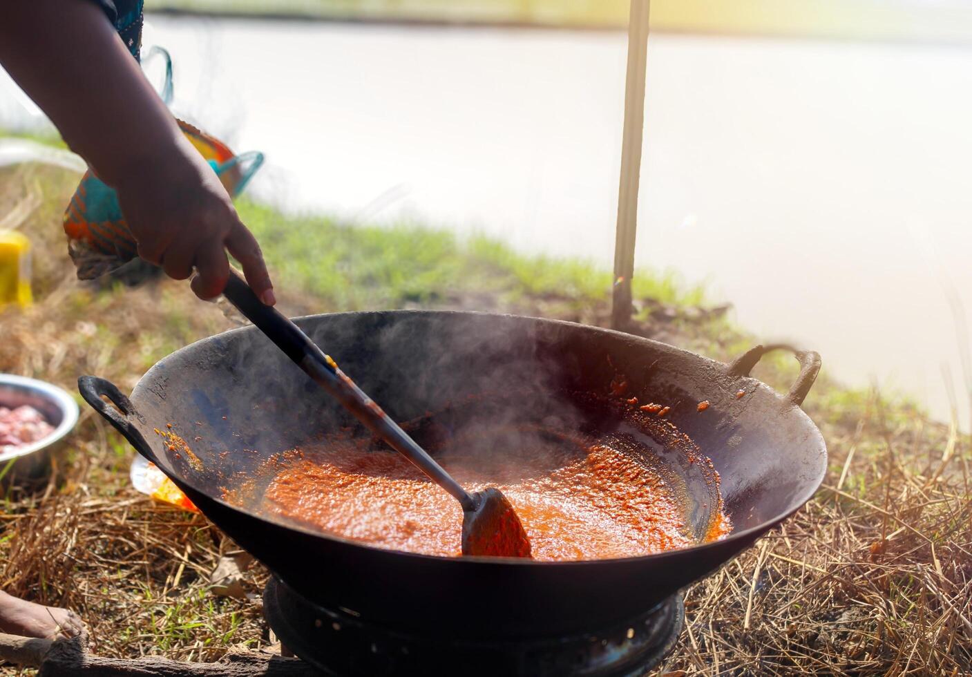 Outdoor Spicy Stir-Fry in Progress. A person stirs a curry seasoning simmering in a large wok over an open fire. photo