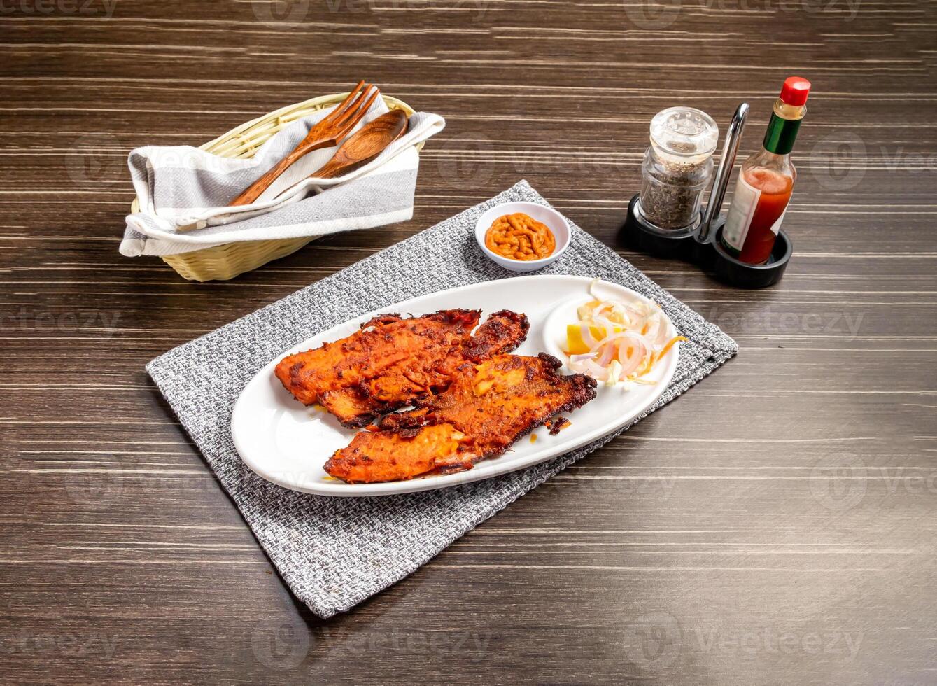 Grilled Fish with Lemon and Onion with chilli garlic sauce served in plate isolated on napkin side view of pakistani and indian spices on wooden background photo