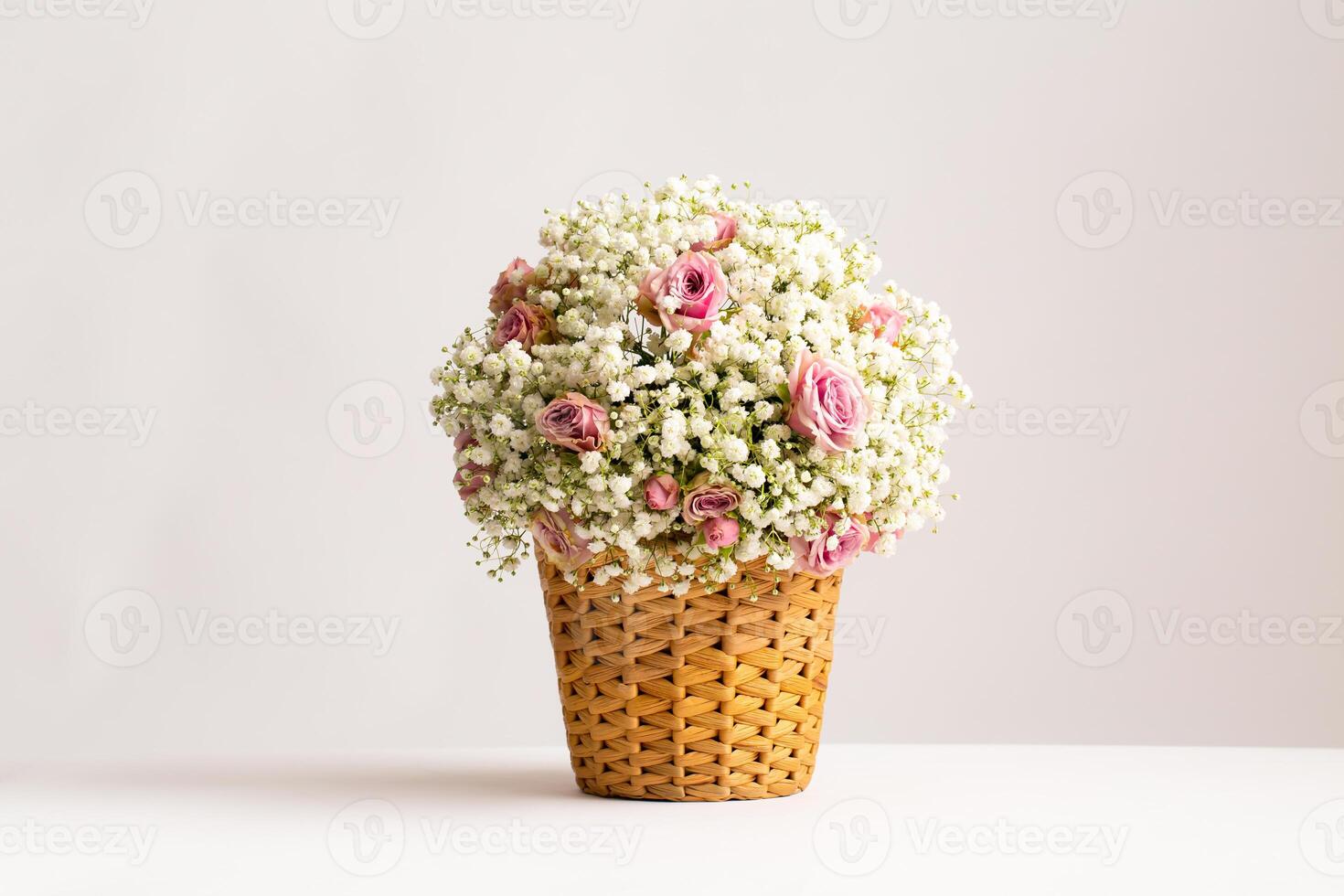 Pink Roses and Baby Breath in Wicker Basket basket filled with a cloud like arrangement of delicate white baby breath flowers arrangement is white background side view beauty of the blooms photo