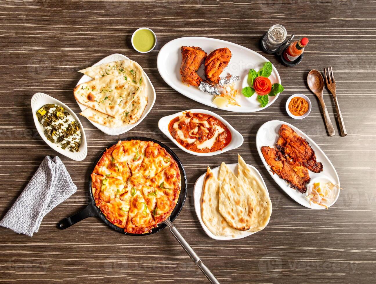Assorted indian spices Palak Paneer, Butter Chicken, Grilled Fish, Tandoori Chicken, Pepperoni Pizza, Naan and chutney served in dish isolated on wooden background top view of pakistani and desi food photo