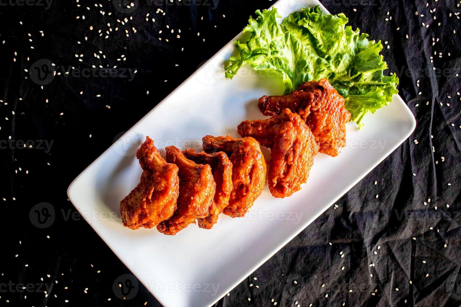 BBQ Chicken Wings garnished with fresh lettuce and sesame seeds served on white plate isolated on dark background top view of fast food photo