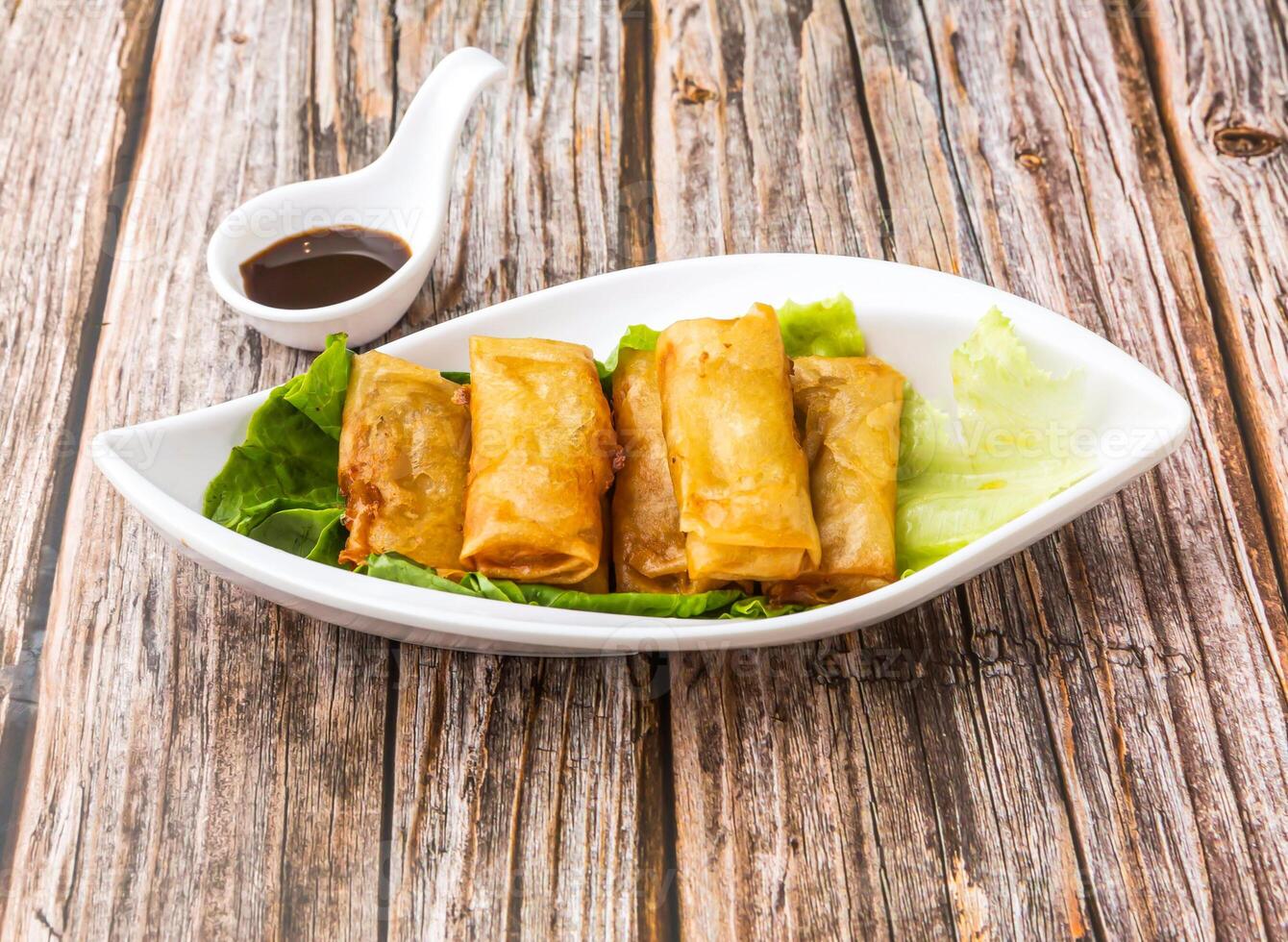 Vegetarian Spring Rolls with lettuce leaves and soy sauce served in dish isolated on wooden table side view of hong kong food photo