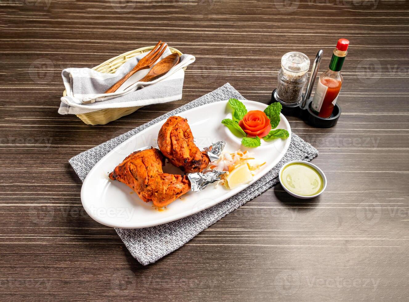 Tandoori Chicken and chutney or raita with Garnishes of lemon and mint leaves served in plate isolated on napkin side view of pakistani and indian spices on wooden background photo