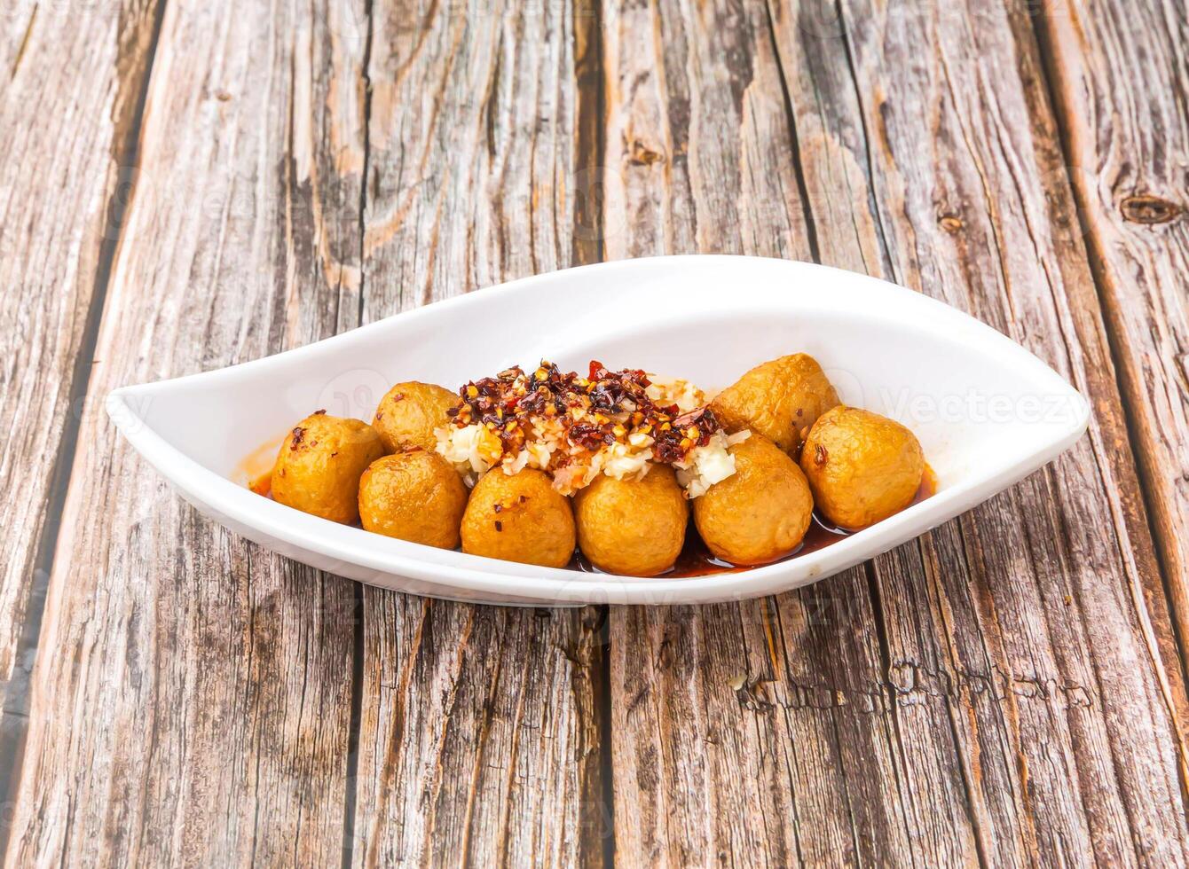 Spicy fried Fish Balls with a spicy chili oil sauce and garnished with chopped garlic served in dish isolated on wooden table side view of hong kong food photo