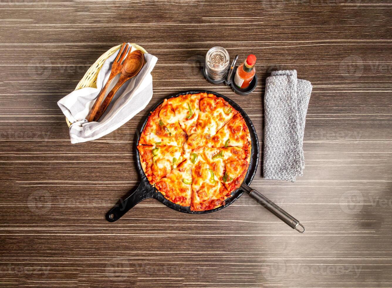 Pepperoni Pizza on Cast Iron Skillet with garlic chilli sauce isolated on wooden background top view of italian fast food photo