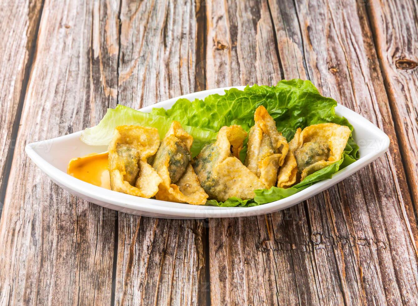 Crispy Fried Wontons with lettuce leaves served in dish isolated on wooden table side view of hong kong food photo