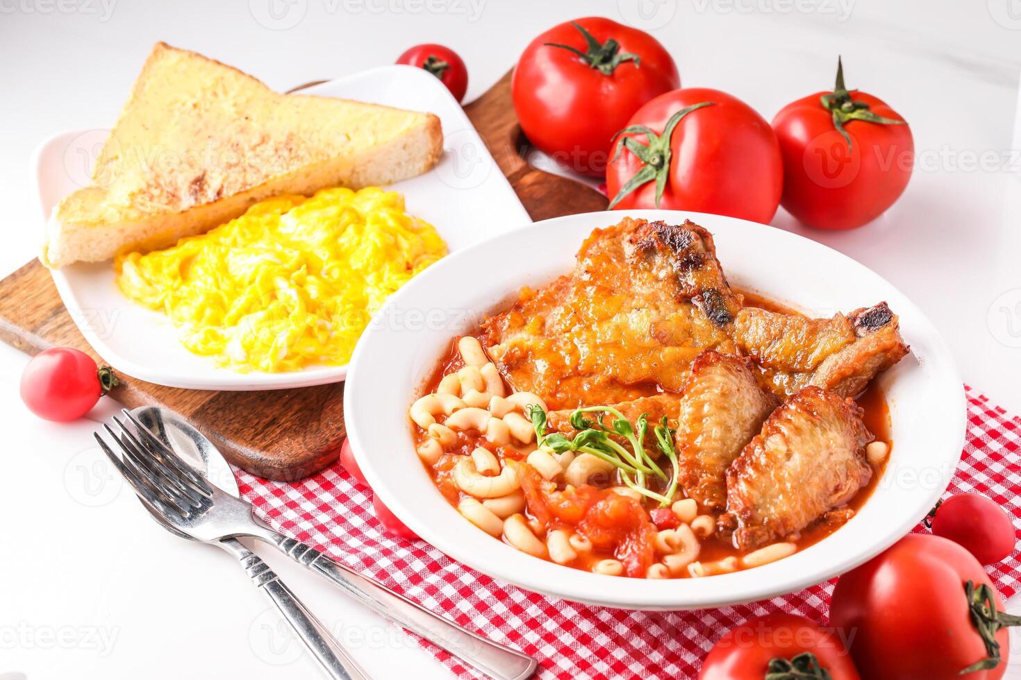 Fresh Tomato Soup with Pork Chop, Chicken Wings, Penne served in bowl alongside scrambled eggs and toast isolated on napkin side view of hong kong food on white background photo