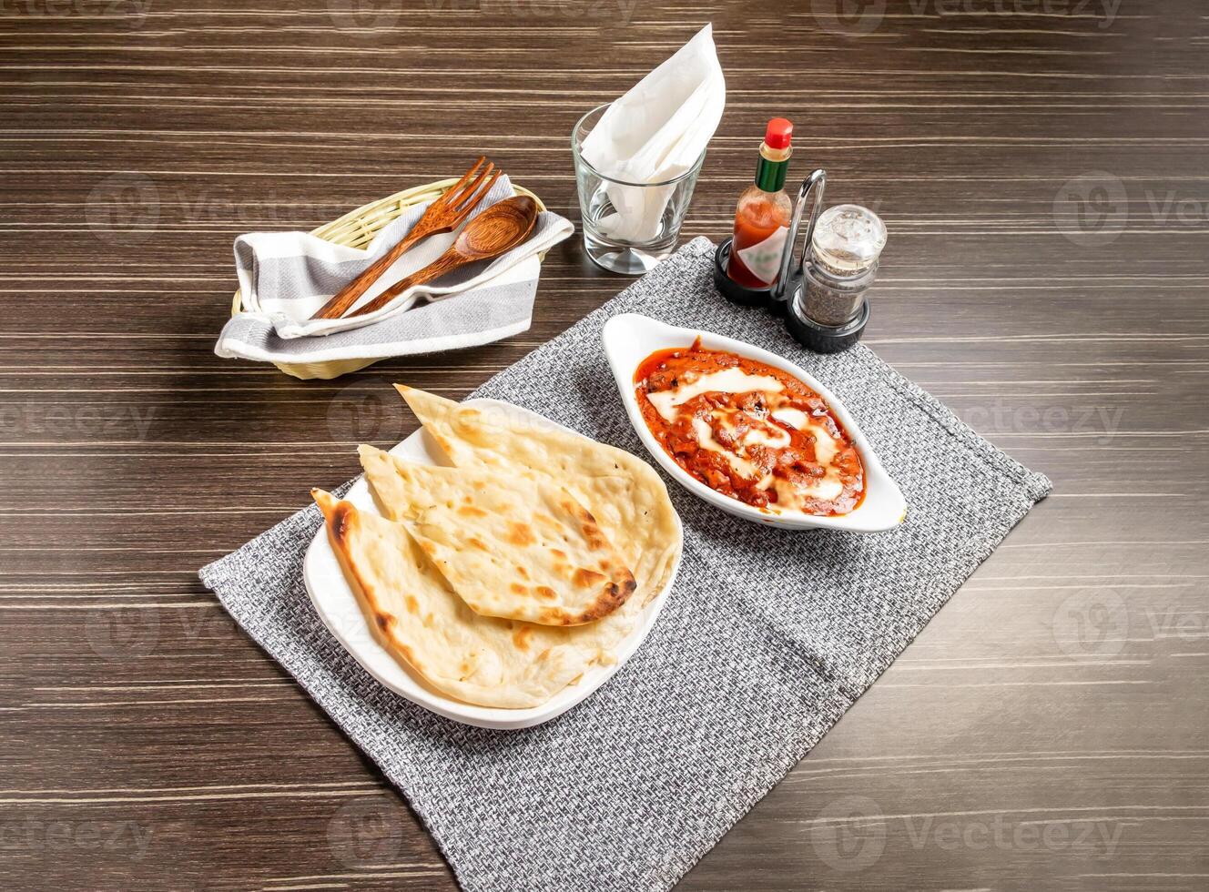 Butter Chicken with Naan served in dish isolated on napkin side view of pakistani and indian spices on wooden background photo