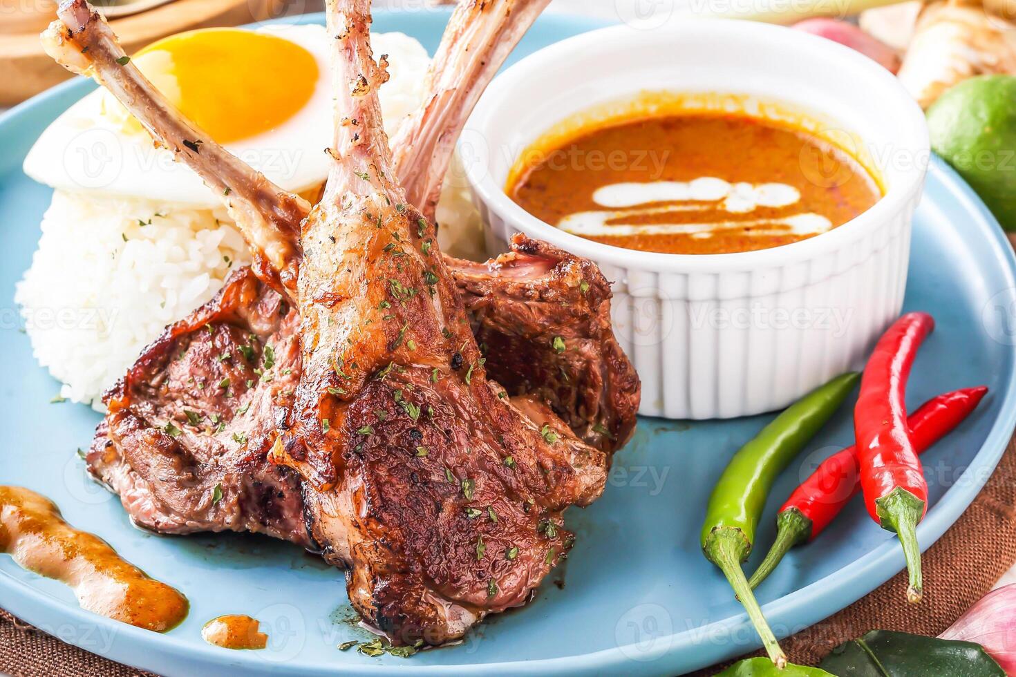 Pan fried Lamb Rack or lamb chops with with curry, rice and sunny side up egg served in plate with chili peppers isolated on napkin closeup side view of hong kong food photo