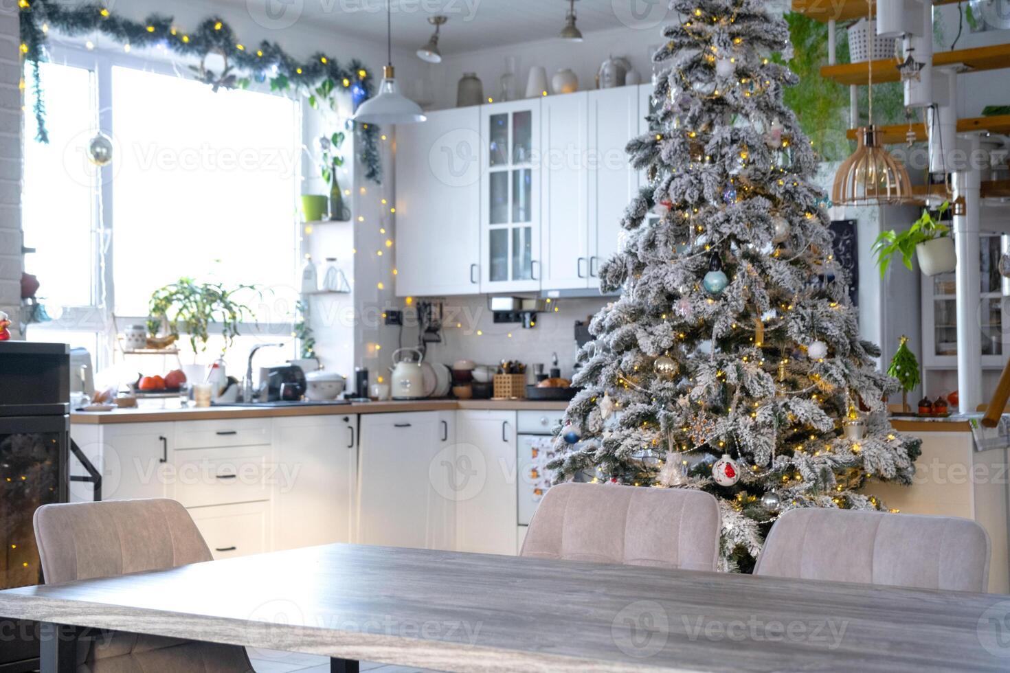 Grey Wooden empty table to demonstrate product with space for text with upholstered chairs in white kitchen, modern interior with Christmas tree and fairy lights. New Year, Christmas mood, cozy home. photo