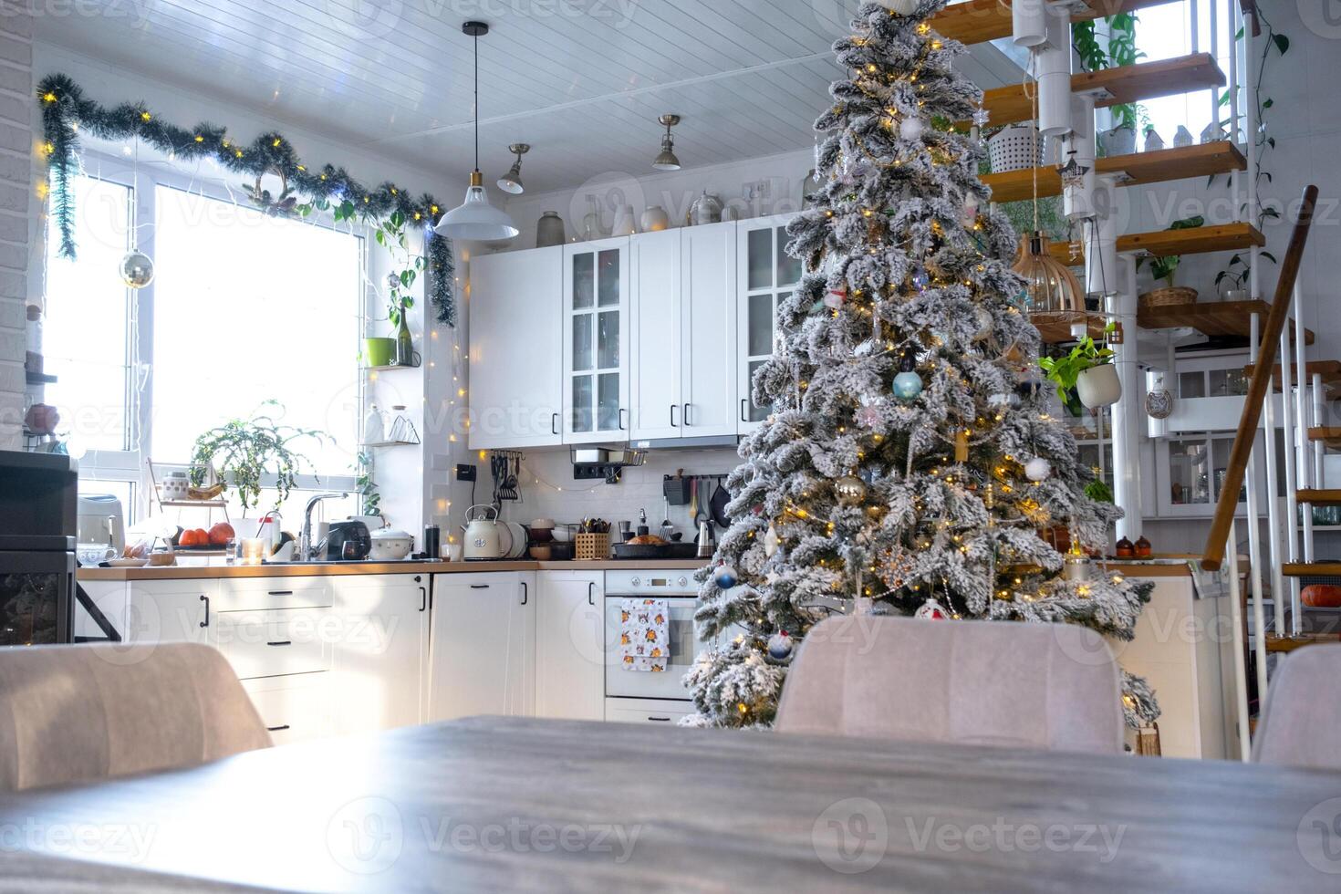 Grey Wooden empty table to demonstrate product with space for text with upholstered chairs in white kitchen, modern interior with Christmas tree and fairy lights. New Year, Christmas mood, cozy home. photo