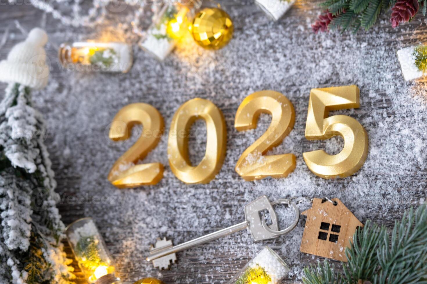 New Year 2025 golden numbers and House key with tiny form of home on festive grey wooden background flatlay, lights of garlands, greeting card. Housing, real estate, relocation, mortgage, insurance photo