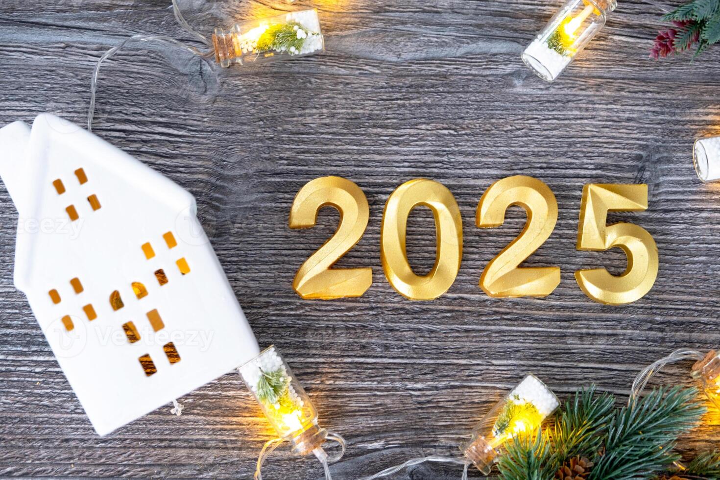 New Year 2025 golden numbers and House key with tiny form of home on festive grey wooden background flatlay, lights of garlands, greeting card. Housing, real estate, relocation, mortgage, insurance photo