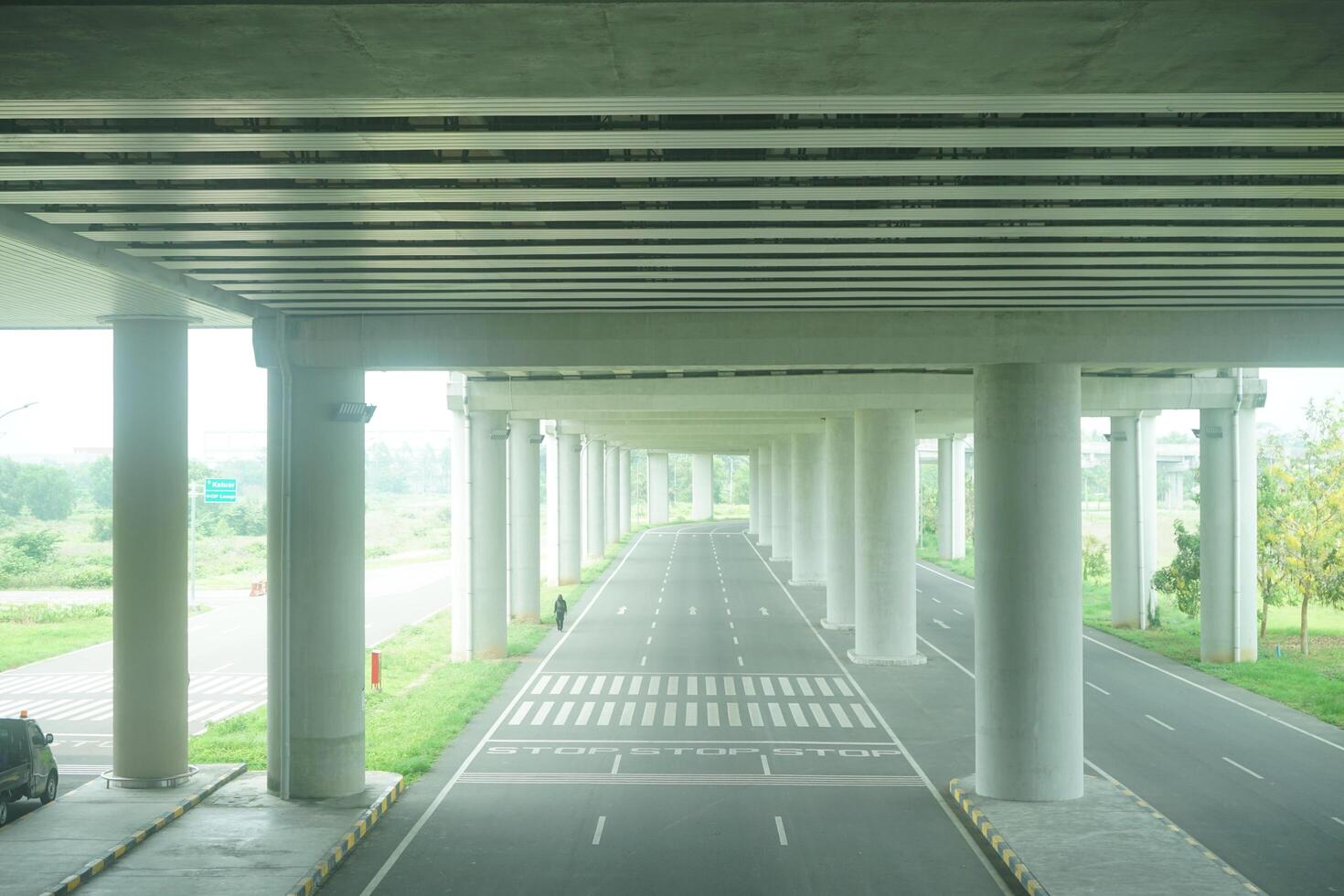 A long, straight road passing through a concrete overpass structure with multiple arched openings, surrounded by green foliage at new yogyakarta international airport photo