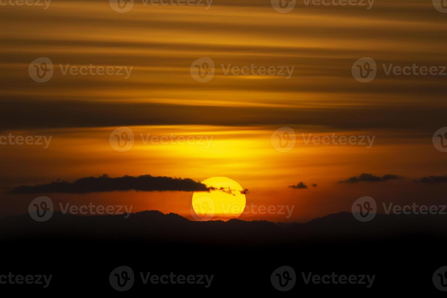 Silhouette mountain with sun and line clouds in sunset sky. photo
