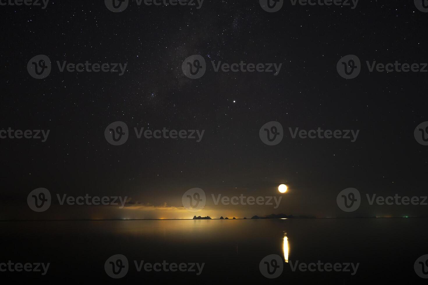 The sky with star and moon is above on light of city and mountain at the lake in dark night. photo