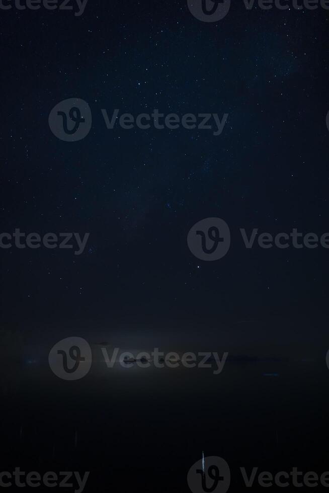 Vertical image of Stardust in the night with noise and grain on the sky with soft light of city in bottom photo