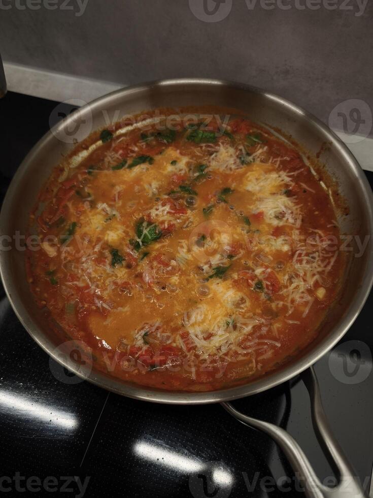 Aromatic tomato sauce cooking in a pan, topped with grated cheese and herbs, creating a flavorful and comforting dish photo