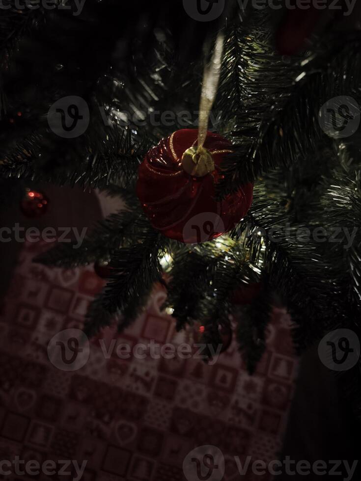Red christmas ball hanging on christmas tree with gift bag below photo