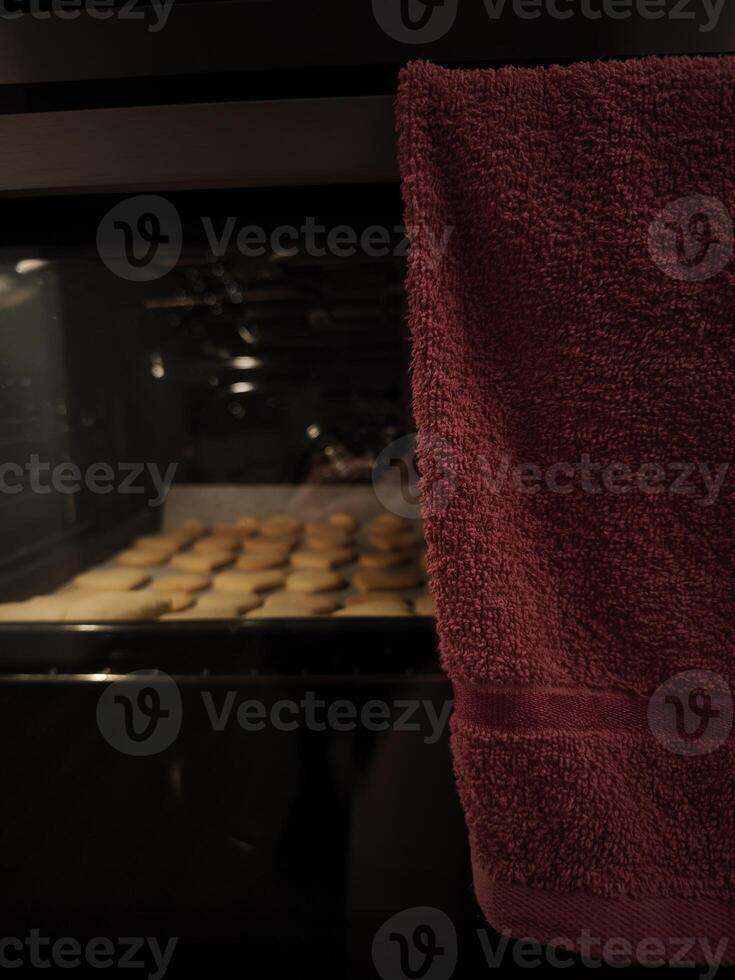 Heart shaped cookies baking in oven for valentine's day with red towel hanging on door photo