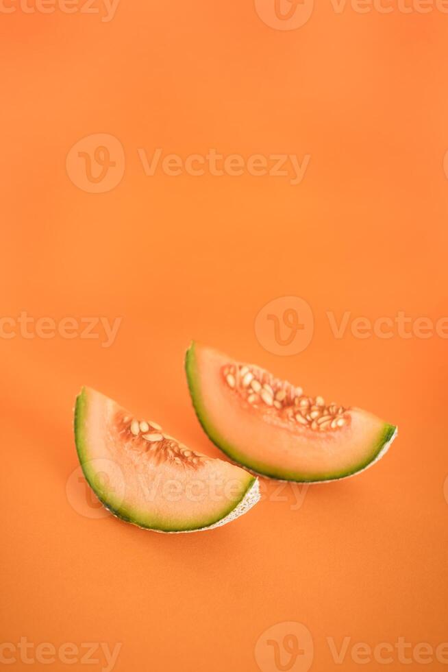 Two slices of melon lie on an orange background. Useful dessert. Place for text. photo
