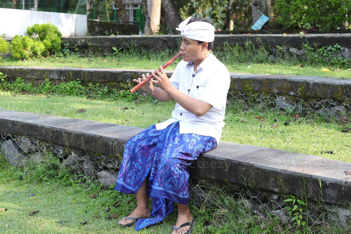 Portrait of Balinese Asian man playing traditional bamboo flute in outdoor park photo