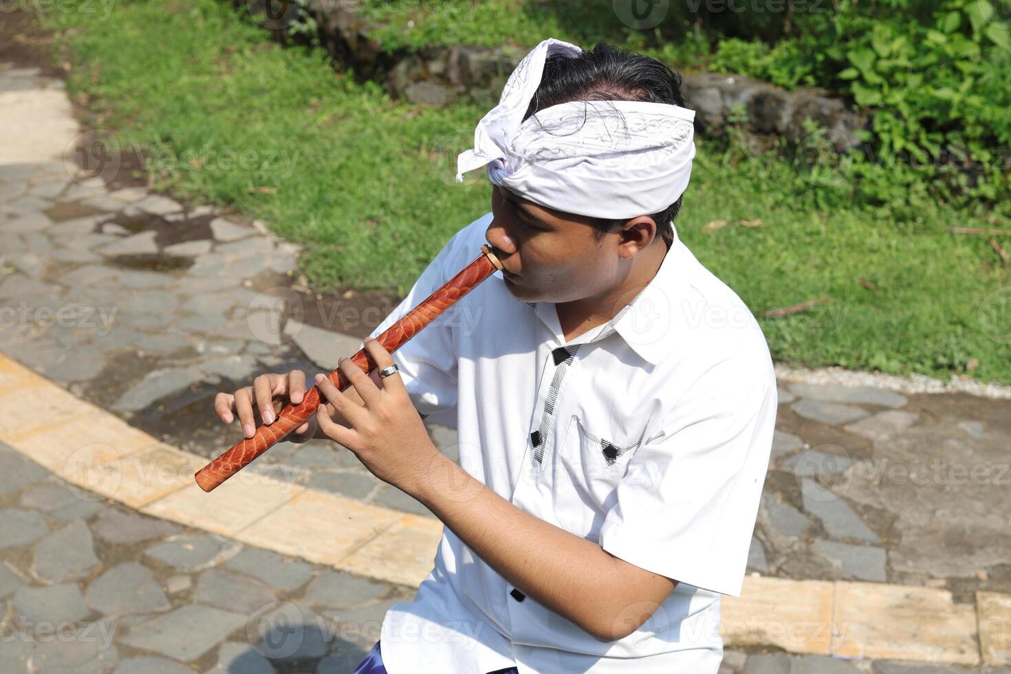 Portrait of Asian man wearing balinese traditional cloth playing bamboo flute in outdoor park photo
