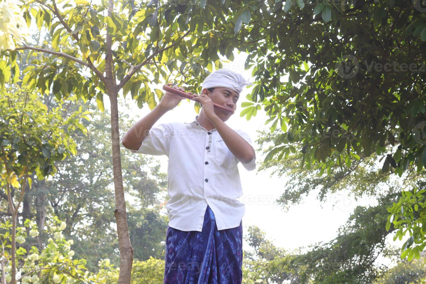 Portrait of Balinese Asian man playing traditional bamboo flute in outdoor park photo