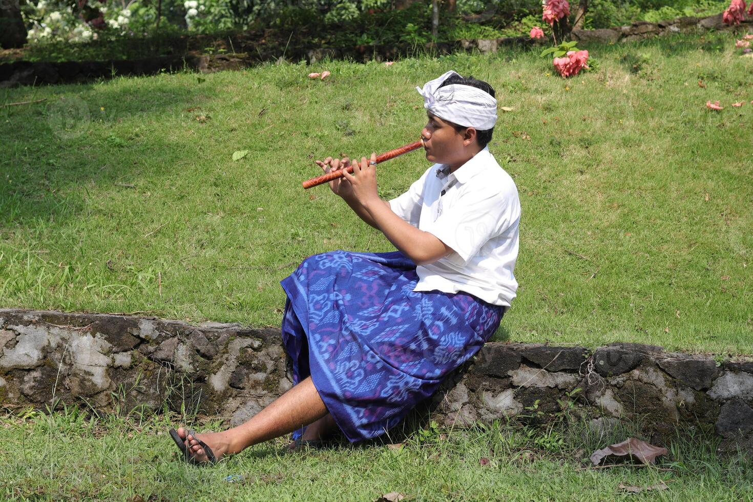 Portrait of Asian man wearing balinese traditional cloth playing bamboo flute in outdoor park photo