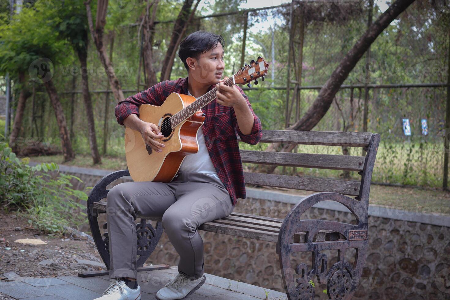 Portrait of Asian man playing guitar in outdoor park photo
