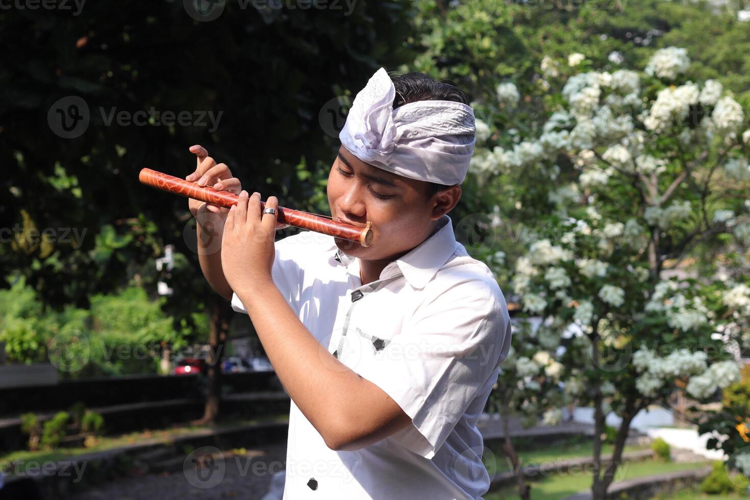 Portrait of Balinese Asian man playing traditional bamboo flute in outdoor park photo