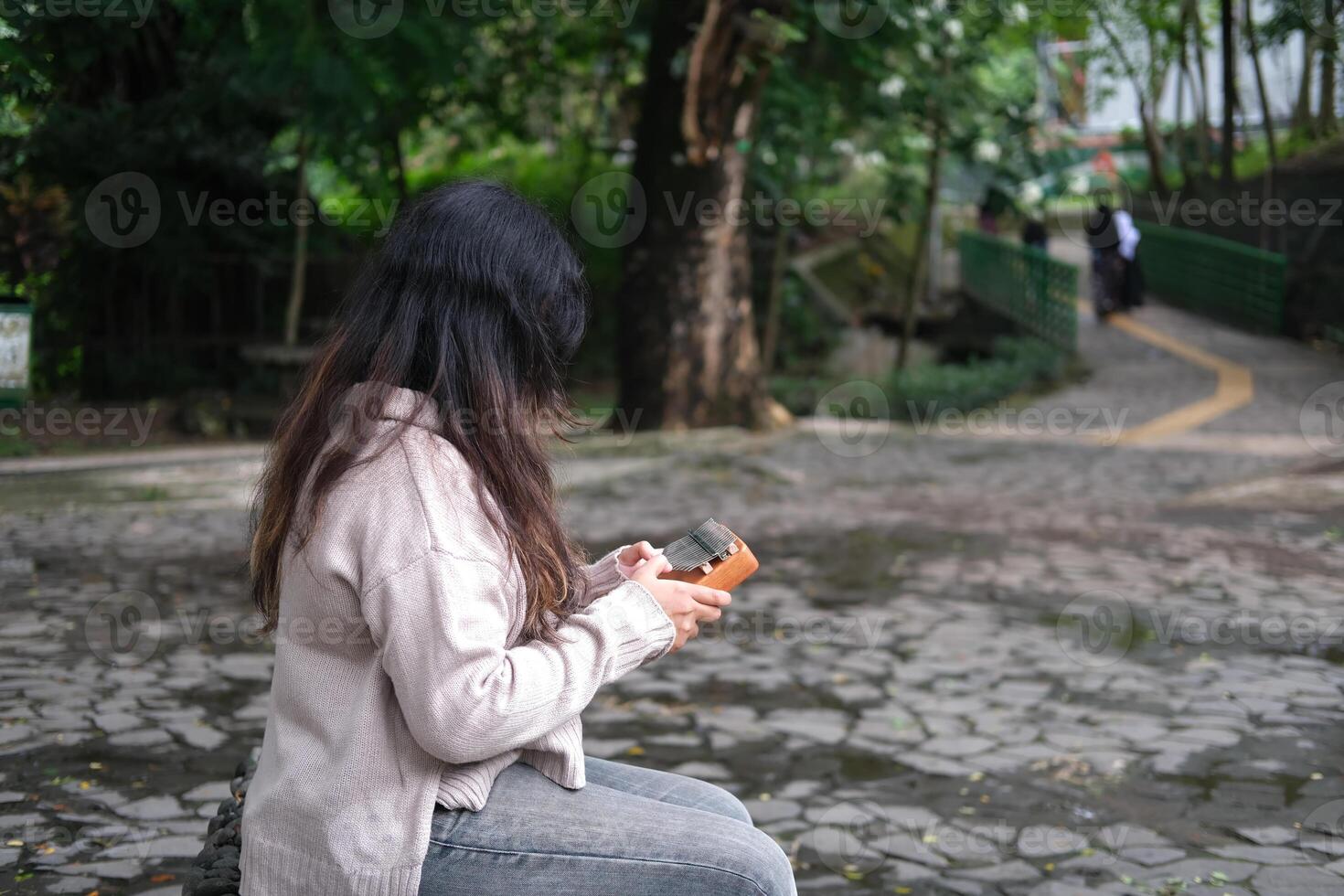 Asian woman plays a kalimba in a green park on a sunny day. The calm melodies and lush leaves create a peaceful and relaxing scene photo