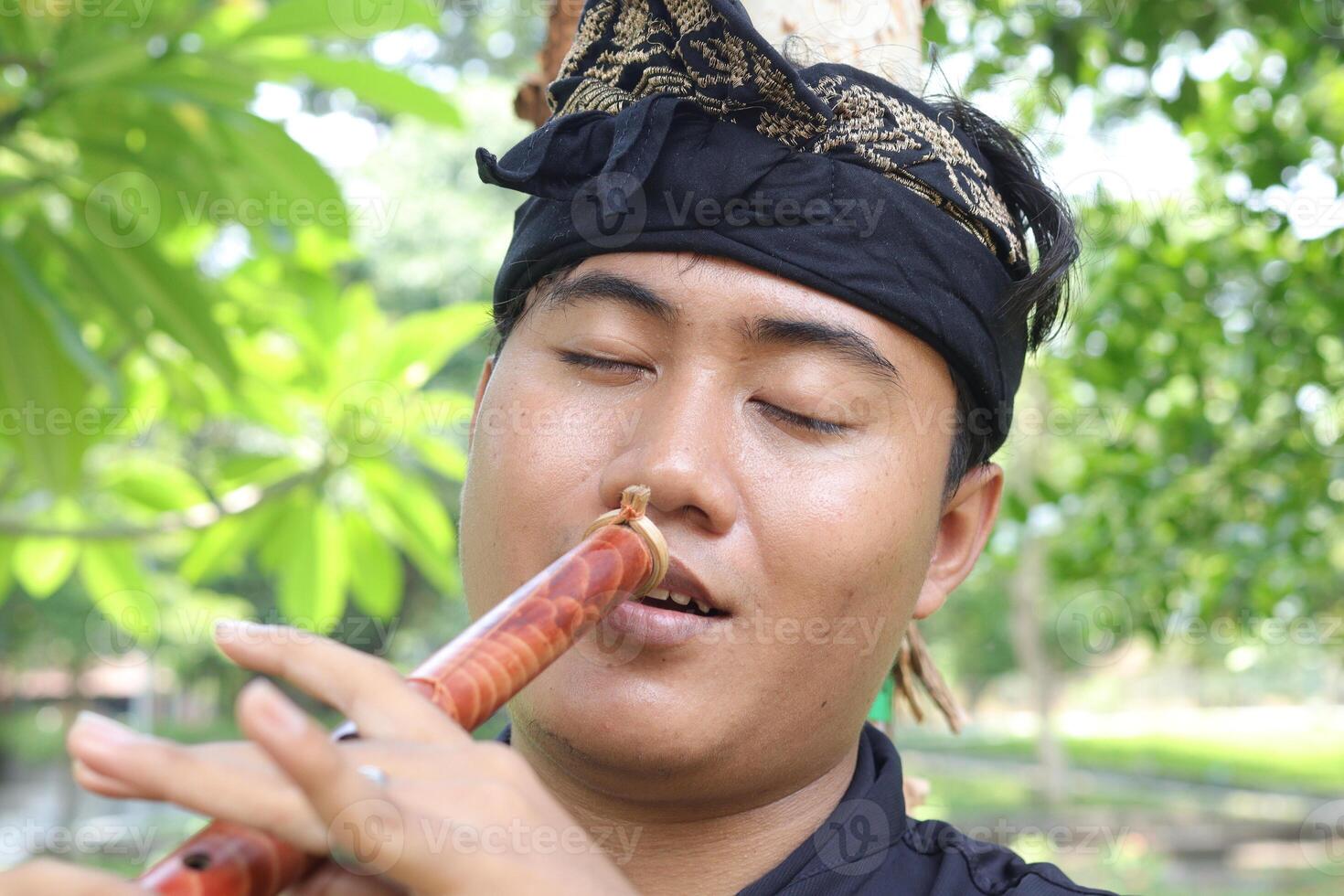 Portrait of Balinese man playing traditional bamboo flute at park in the morning photo
